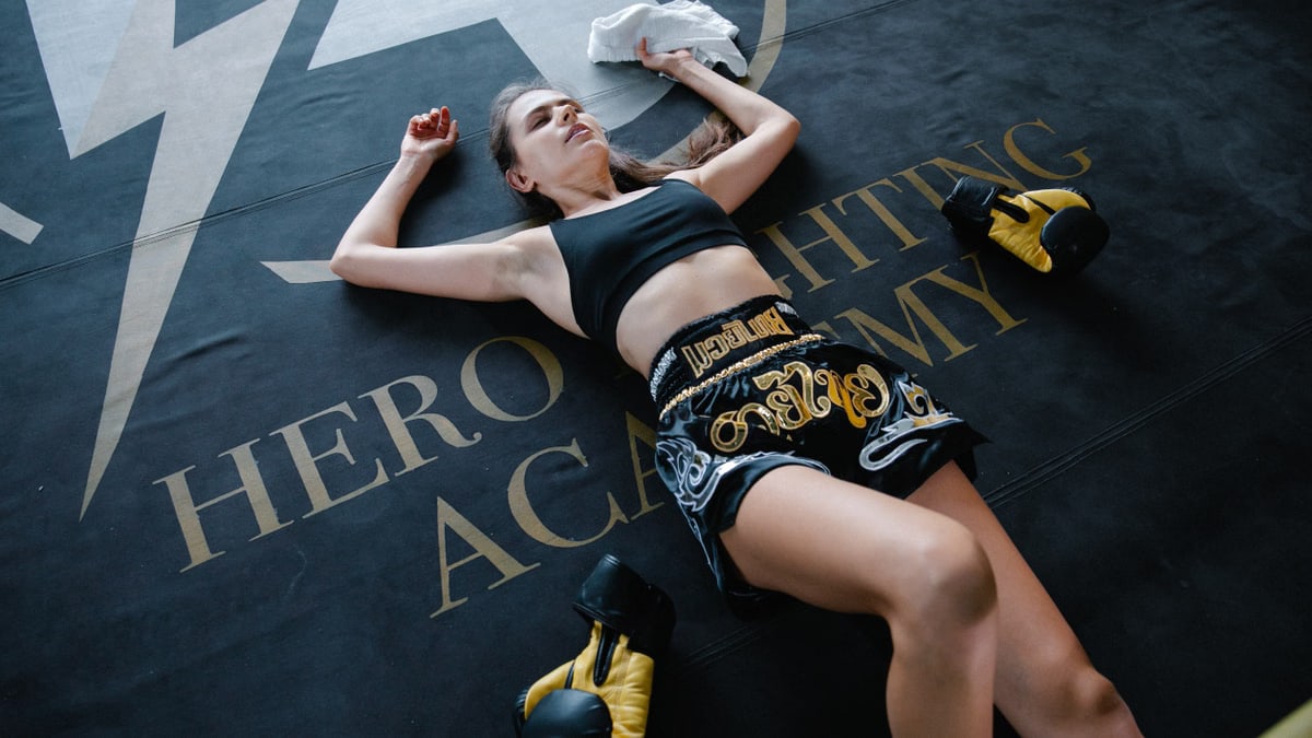 A woman in sportswear resting on a boxing mat after a workout at Hero Fighting Academy.